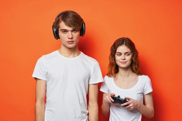 Mladý pár v bílém trička s joysticks hrát konzole oranžové pozadí — Stock fotografie