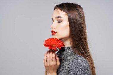 Yüzüne yakın kırmızı çiçekli güzel bir kadın. Parlak makyajlı.