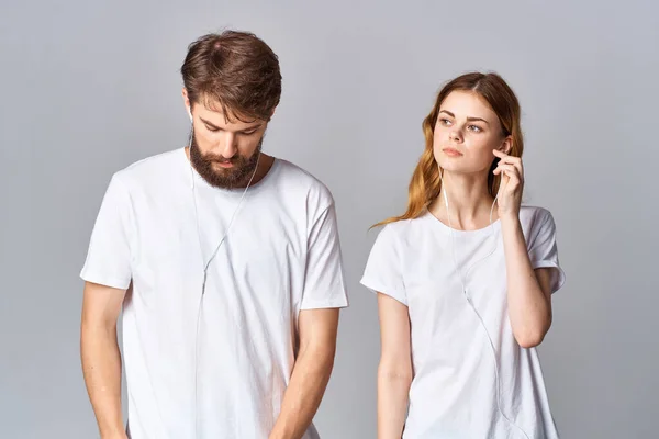 Hombre y mujer en camisetas blancas música en auriculares fondo claro — Foto de Stock