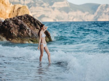 Beyaz mayo giymiş bir kadın kıyıda yürüyor. 