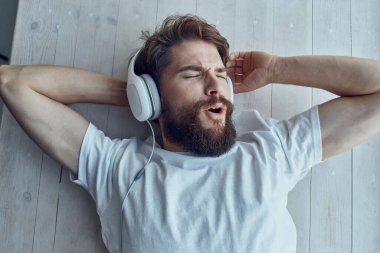 Sakallı adam pencere eşiğinde uzanıyor, kulaklık takıyor.