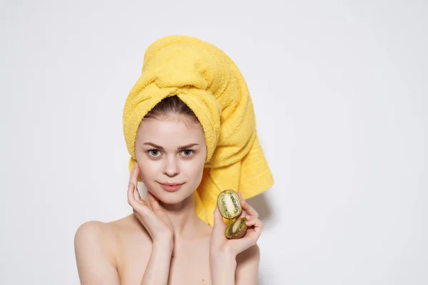 Kvinna med bara axlar med en gul handduk på huvudet kiwi i händerna ren hud — Stockfoto