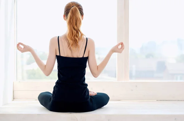 Lotus pozisyonunda oturan kadın pencerenin yanında meditasyon yoga yapıyor. — Stok fotoğraf