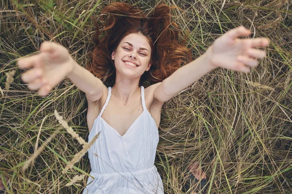 Mujer alegre en un vestido blanco con sus brazos levantados miente en la hierba —  Fotos de Stock