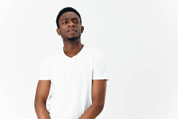 A pretty African guy in a white T-shirt looks to the side on a light background Copy Space. High quality photo