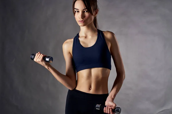 Mujer atlética con una figura delgada con mancuernas en las manos de entrenamiento de fitness — Foto de Stock