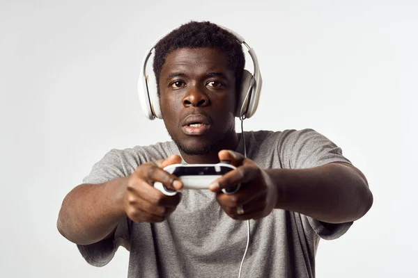 Un hombre de apariencia africana en auriculares con un mando en sus manos juega tecnología de videojuegos — Foto de Stock