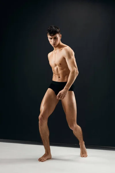 Sexy man with naked muscular body in black panties dark background — Stock Photo, Image