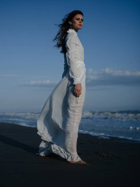 Beyaz elbiseli güzel bir kadın okyanus manzarasında yürüyor.