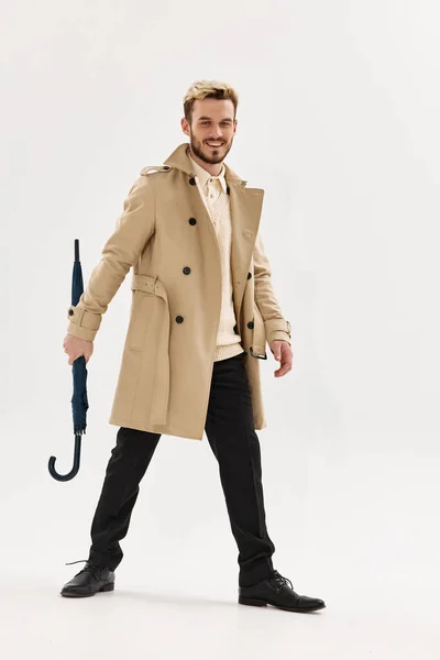 Веселий чоловік в бежевому пальто парасолька в руках чоловіча студія моди ізольований фон — стокове фото