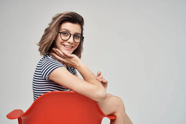 Schöne Frau mit Brille sitzt auf dem roten Stuhl posiert Studio — Stockfoto