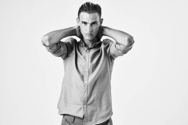 Havalı saç stili olan yakışıklı bir adam ellerini arka planda tutarak poz veriyor.