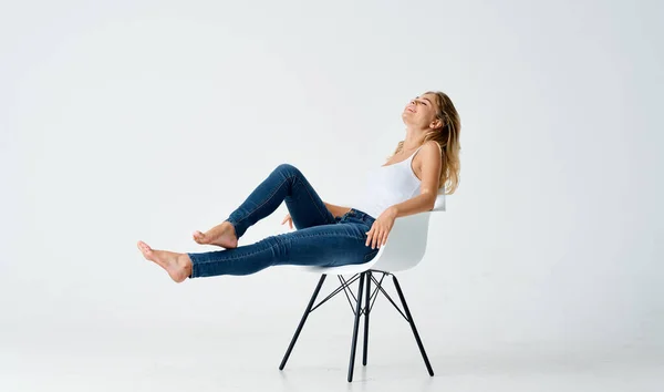 Mulher de jeans sentado em uma cadeira branca emoção casa isolado fundo — Fotografia de Stock