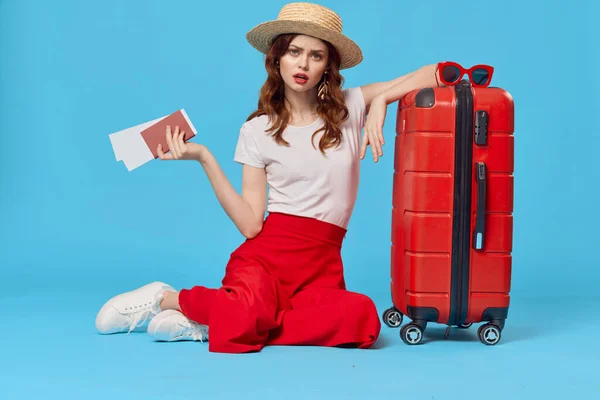 모자를 쓴 쾌활 한 여자가 빨간 여행 가방을 타고 바닥에 앉아 있습니다. — 스톡 사진