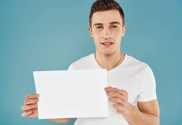 handsome man in white t-shirt with white sheet of paper in his hands paperspace blue background