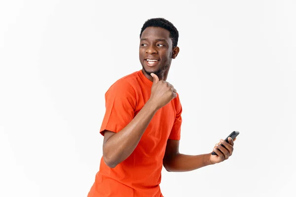 Африканский мужчина в оранжевой футболке оглядывается назад и держит в руке мобильный телефон. — стоковое фото