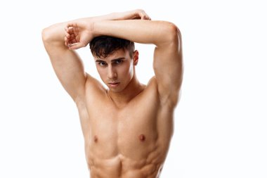 Çıplak gövdeli yakışıklı sporcu ellerini kafasının arkasında tutuyor.