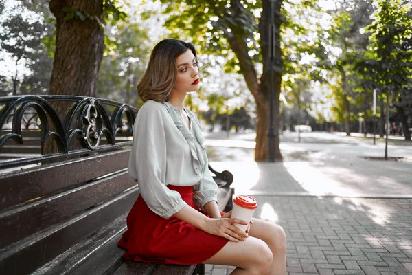 Hezká žena sedí na lavičce v parku venku šálek kávy — Stock fotografie