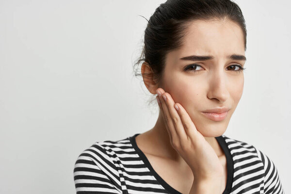 brunette in striped t-shirt holding face toothache discontent health problem