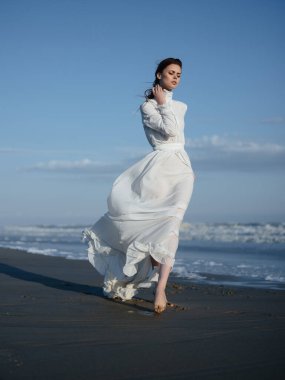 Beyaz elbiseli kadın plaj tatilinde yürürken poz veriyor.
