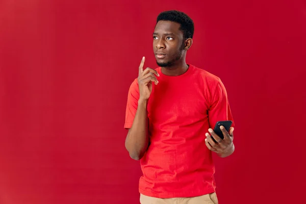 Homem de aparência africana em uma camiseta vermelha com um telefone em suas mãos — Fotografia de Stock