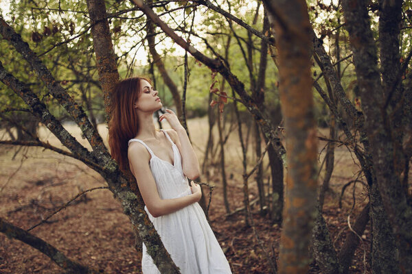 Pretty woman in white dress leaning against a tree nature summer. High quality photo
