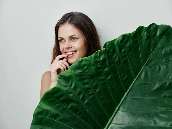 Mulher sorridente com uma grande folha verde em um fundo exótico luz — Fotografia de Stock