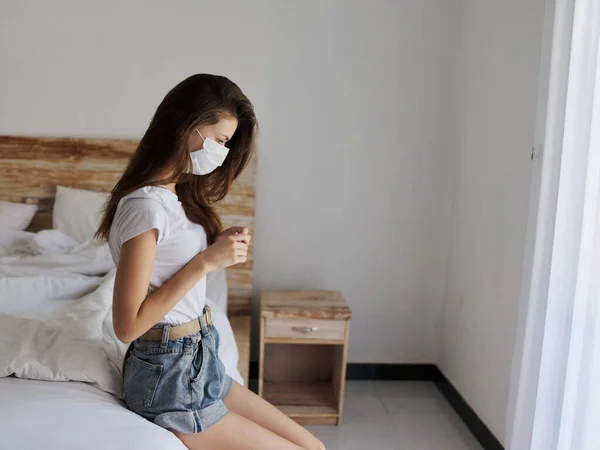 Žena na dovolené sedí na posteli vnitřní police lékařská maska pandemická karanténa — Stock fotografie