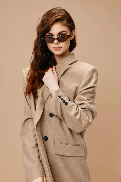 Mulher de casaco e óculos de sol no fundo bege vista frontal — Fotografia de Stock