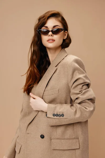 Красива жінка в окулярах і в куртці на бежевому фоні зачіски модель — стокове фото