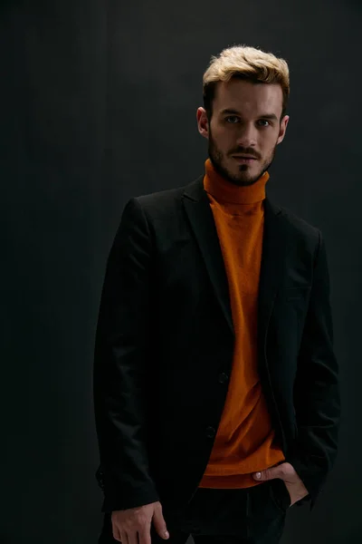 Hombre rubio en un abrigo y un suéter naranja en un modelo de vista frontal de fondo oscuro —  Fotos de Stock