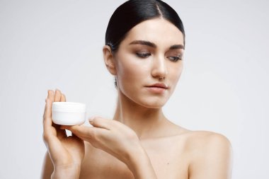 Çıplak omuzlu kadın krem kavanozu cilt bakımını nemlendiriyor.