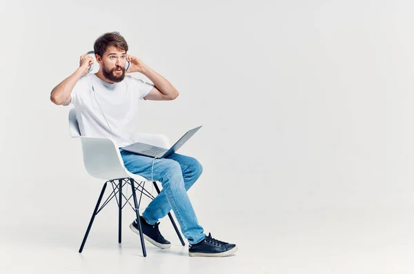 Mężczyzna w białej koszulce siedzi na krześle z laptopem w słuchawkach — Zdjęcie stockowe