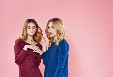 Elbiseli şirin kızlar arkadaşlığın pembe arka planında duruyorlar.