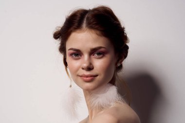 Çıplak omuzlu, parlak makyajlı, kabarık küpeli, hafif moda arka planlı bir kadın.