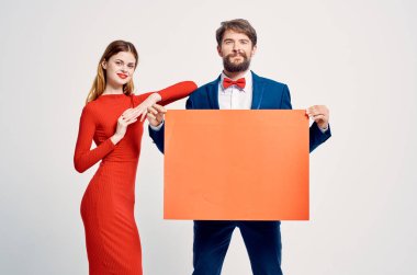 Kırmızı elbiseli bir kadının yanında takım elbiseli bir adam reklam sunumu yapıyor.