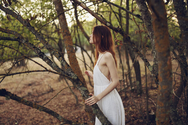 Pretty woman in white dress leaning against a tree nature summer. High quality photo