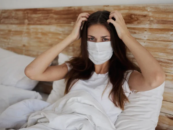 Una donna in maschera medica si trova a letto su un cuscino pandemia quarantena coronavirus — Foto Stock