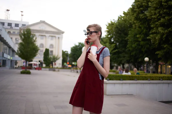 Una donna con gli occhiali cammina per la città un bicchiere con una bevanda di comunicazione per il tempo libero — Foto Stock
