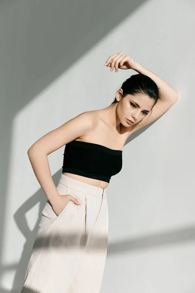 Beyaz pantolonlu ve siyah bluzlu genç bir bayan elini duvara yaslıyor. — Stok fotoğraf
