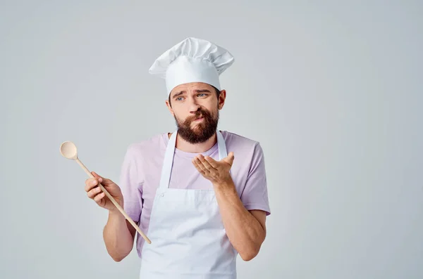 Chef masculino em um avental branco com um boné na cabeça com uma colher em suas mãos preparando comida — Fotografia de Stock