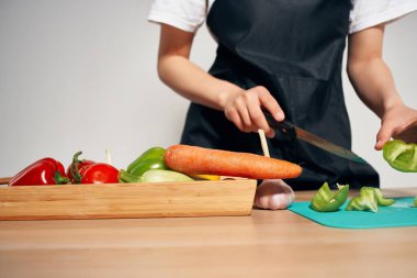 Siyah önlüklü kadın mutfakta sebze doğruyor ve yemek hazırlıyor.