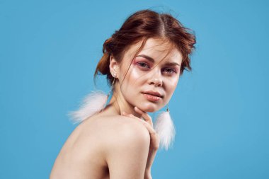 Çıplak omuzlu, parlak makyajlı, mavi arka planlı bir kadın.