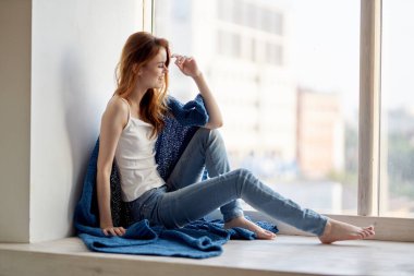 Pencerenin yanında oturan mavi ekose gülüşlü kadın.