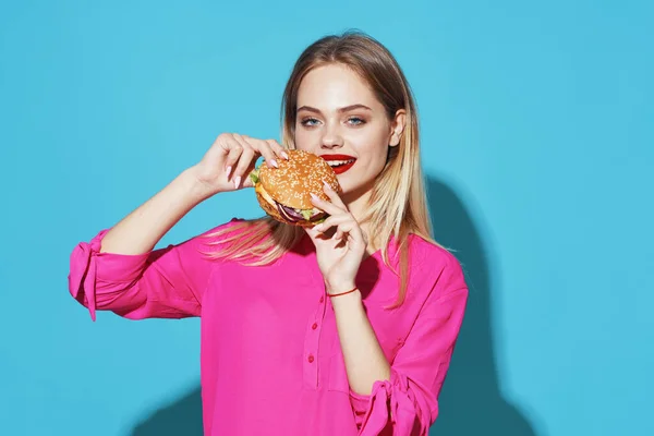 Веселая блондинка в розовой рубашке гамбургер быстрого питания закуски синий фон — стоковое фото