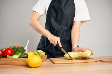 Siyah önlüklü bir kadın sebze doğruyor. Mutfakta yemek pişiriyor.