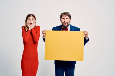 Kırmızı elbiseli bir kadının yanında takım elbiseli bir adam. Sarı model poster reklamı.