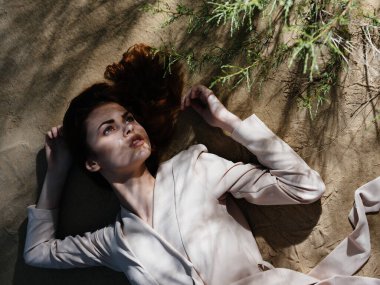 Palto giymiş güzel bir kadın yaz mevsiminde yerde yatıyor.