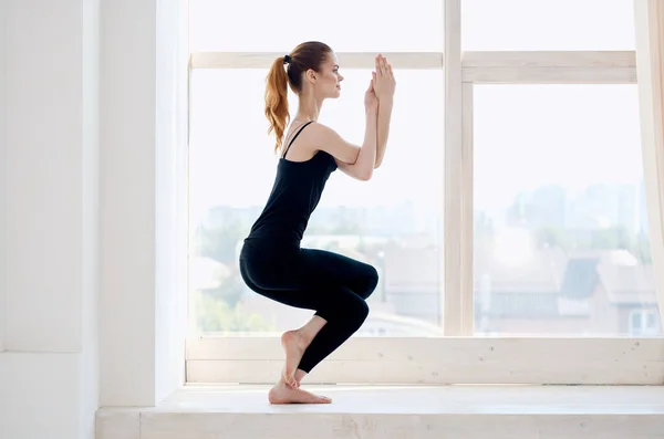 Женщина осуществляет около окна йога asana медитации — стоковое фото