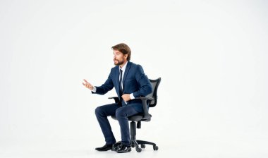 Ofis sandalyesinde oturan takım elbiseli sakallı bir adam.